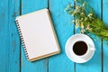 Top view image of daisy flowers, blank notebook next to cup of coffee on blue wooden table.