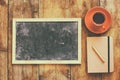 Top view image of empty blackboard next to cup of coffee and notebook, over wooden table. image with retro style filter Royalty Free Stock Photo