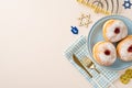 Top-view image featuring customary Jewish delicacies sufganiyot, napkin, cutlery, Star of David, menorah, gelt on beige surface