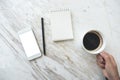 A hand holding coffee cup with a white mobile phone with blank desktop screen and empty notebook on table Royalty Free Stock Photo