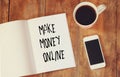 Top view image of open note book with the phrase make money online, next to cup of coffee and smartphone.