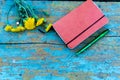 Top view image of open notebook on the old blue painted wooden table with yellow flowers. Blank notebook with flower and green pen Royalty Free Stock Photo