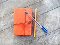 Top view image of orange vintage notebook with pen and pencil on wooden table. Diary writing concept. Flat lay