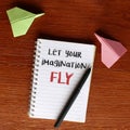 Top view image of paper plane and notebook with text LET YOUR IMAGINATION FLY
