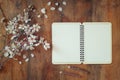 Top view image of spring white cherry blossoms tree next open blank notebook on wooden table. vintage filtered and toned image