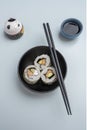 Top view image of sushi slices, uramaki, inside a black Japanese bowl, black chopsticks, soy sauce and a smiling cat figure on a Royalty Free Stock Photo