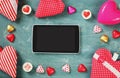 Top view image of tablet, colorful heart shape chocolates, fabric hearts on blackboard background