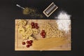 Top view image of a variety of Italian raw pasta, wheat flour, oregano, cherry tomatoes and bamboo table on black background