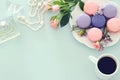 Top view image of white cup of coffee, perfume, white pearls and colorful macaron or macaroon over pastel wooden background.