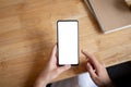 top-view image of a white-screen smartphone mockup in a woman's hand above a wood table Royalty Free Stock Photo