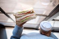 A woman holding and eating whole wheat sandwich and coffee in the morning