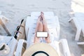 A woman holding and using white mobile phone with blank desktop screen while laying down on beach chair Royalty Free Stock Photo