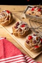 Top view of individual plum cakes, decorated with sugar, raisins and cherries, on wooden table with rustic red cloth, Royalty Free Stock Photo