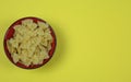 Top view on isolated red bowl with farfalle noodles on yellow background with blank copy space for text