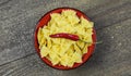Top view on isolated red bowl with raw italian farfalle noodles and fresh chilli pepper on wood table