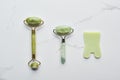 Top view of jadeite facial rollers and spatula on marble surface.