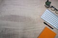 Top view keyboard, eyeglasses and notebook on wooden desk.