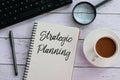 Top view of keyboard,magnifying glass,pen,coffee and notebook written with Strategic Planning.