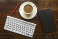 Top view of keyboard, pencil, black notebook and a cup of coffee on a wooden table. Royalty Free Stock Photo