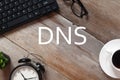 Top view of keyboard,sunglasses,a cup of coffee,clock and plant on wooden background written with DNS