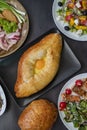 Top view of khachapuri dish with cheese and egg in Adjarian with Caesar and Greek salads with potatoes and herring Royalty Free Stock Photo