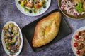 Top view of khachapuri dish with cheese and egg in Adjarian with Caesar and Greek salads with potatoes and herring Royalty Free Stock Photo