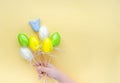 Top view of kids hand holding bouquet of multicolored eggs and smiling tulip on a bright yellow background. Easter greeting card