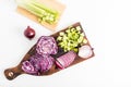 top view of the kitchen wooden board with chopped red cabbage, purple onions, a stalk of fresh celery. white background.