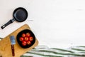 Top view of knife, small pan and fresh ripe cherry tomatoes in small black bowl on a rustic white wooden table. Ingredients and Royalty Free Stock Photo