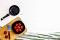 Top view of knife, small pan and fresh ripe cherry tomatoes in small black bowl on a rustic white wooden table. Ingredients and Royalty Free Stock Photo