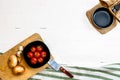 Top view of knife, small pan, onions, garlic and fresh ripe cherry tomatoes in small black bowl on a rustic white wooden table. Royalty Free Stock Photo