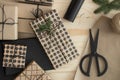 Top view of a kraft and black christmas gifts surrounded with scissors, leaves and twine on a wooden table