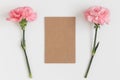 Top view of a kraft card mockup with pink carnations on a white table