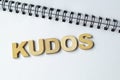 Top view of KUDOS wooden letters on white notepad. Royalty Free Stock Photo