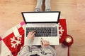 Top view of laptop in girl`s hands sitting on a wooden floor with cup of coffee, christmas decoration, gifts and wrapping paper Royalty Free Stock Photo