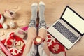 Top view of laptop in girl`s hands sitting on a wooden floor with cup of coffee, christmas decoration, gifts and wrapping paper Royalty Free Stock Photo