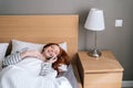 Top view of laughing young woman lying on cosy bed at home and talking mobile phone after waking up in morning at home. Royalty Free Stock Photo