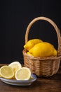 Top view of lemons in basket with handle and plate with half lemons on wooden table and black background, vertically Royalty Free Stock Photo