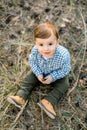 Top view of little baby boy in checkered shirt, sitting in autumn pine forest, playing with cone and smiling to camera Royalty Free Stock Photo