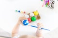 Top view of little girl holding paintbrush and decorating Easter eggs with blue watercolor over white table