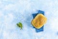 Top view of loaf of freshly baked bread with parsley on linen towel over light blue concrete background