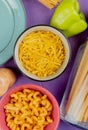 top view of macaronis as cavatappi bucatini tagliatelle with pepper and plate on purple background