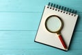 Top view of magnifier glass and empty notebook on blue wooden background, space for text. Find keywords concept