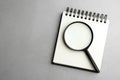 Top view of magnifier glass and empty notebook on  grey stone background, space for text. Find keywords concept Royalty Free Stock Photo