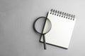 Top view of magnifier glass and empty notebook on grey stone background, space for text. Find keywords concept Royalty Free Stock Photo