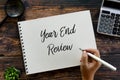 Top view of magnifying glass,calculator,plant,pen and hand writing ` Year End Review ` on a notebook on wooden background