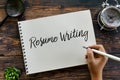 Top view of magnifying glass,clock,plant,pen with hand writing & x27; Resume Writing & x27; on a notebook on wooden background