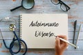 Top view of magnifying glass,glasses,stethoscope,pen and hand writing ` Autoimmune Disease ` on notebook on wooden background