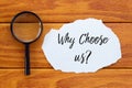 Top view of magnifying glass and piece of paper written with question Why Choose Us? on wooden background.