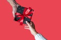 top view of male and female hands holding a gift box with red ribbon on red background. Royalty Free Stock Photo